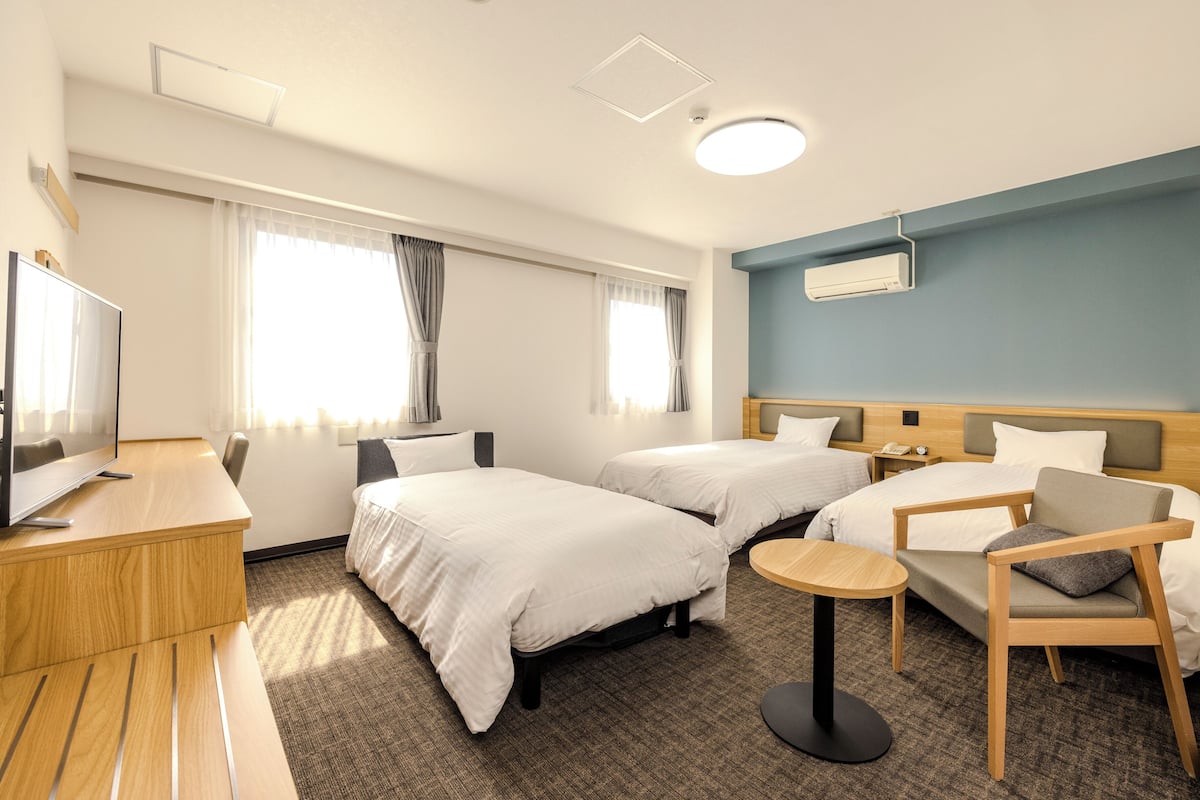 Een hotelkamer met twee bedden, een bureau, een stoel, een klein tafeltje en een televisie.