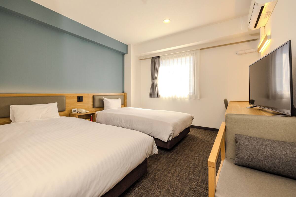 Een hotelkamer met twee bedden, een televisie, een bureau en een raam met gordijnen.