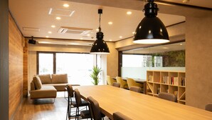 A modern meeting room with a long wooden table, comfortable seating, and a bookshelf. - Kochi Sunrise Hotel (Kochi)