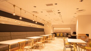 A modern dining area with multiple tables and chairs, a long bench, and a kitchen area in the background. - Kochi Sunrise Hotel (Kochi)