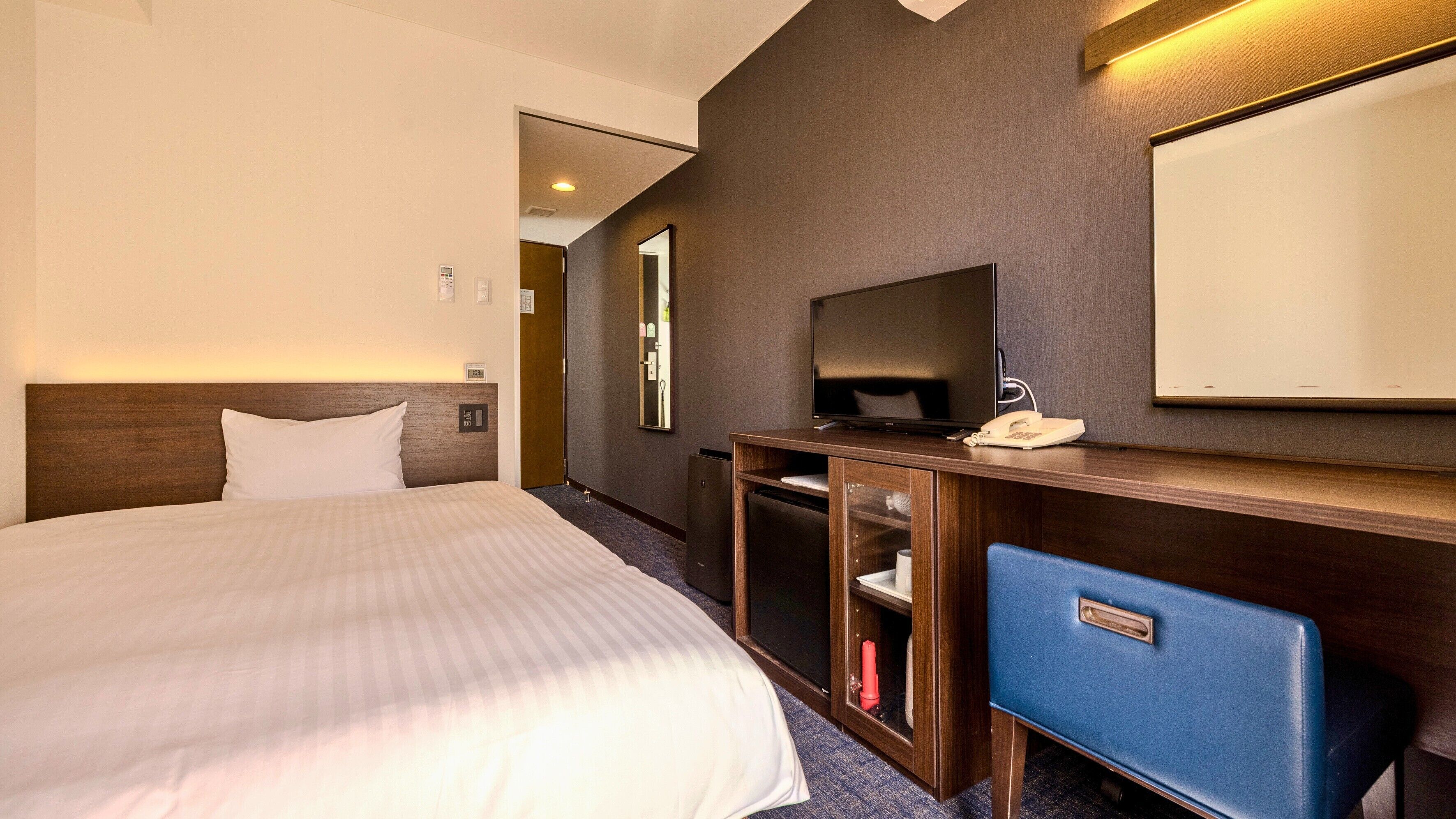 Ein Hotelzimmer mit einem Bett, einem Fernseher, einem Schreibtisch mit Telefon und einem Spiegel.