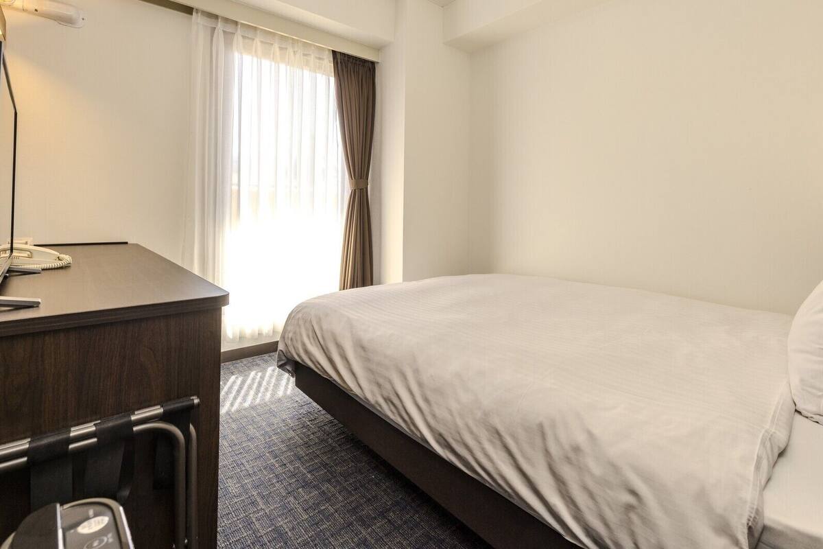 Een hotelkamer met een bed, een bureau met telefoon en een raam met gordijnen.