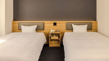 A hotel room with two beds, a wooden headboard, a nightstand with a phone and clock, and a dark carpet.