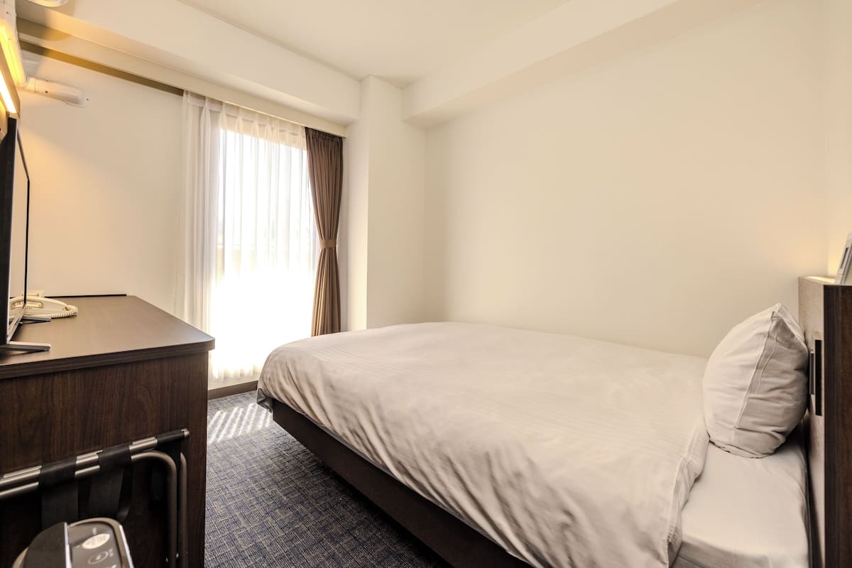 Een hotelkamer met een bed, een bureau, een stoel, een telefoon en een raam met gordijnen.