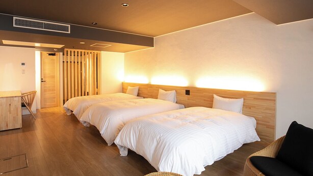 A hotel room with two beds, a wooden headboard, a wicker chair, and a desk. - Kochi Sunrise Hotel (Kochi)
