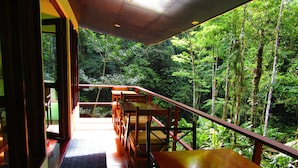 A balcony with wooden tables and chairs, overlooking a dense forest. - Agua Inn (Arenal)