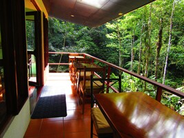 Un balcón con mesas y sillas de madera, con vista a un bosque frondoso.