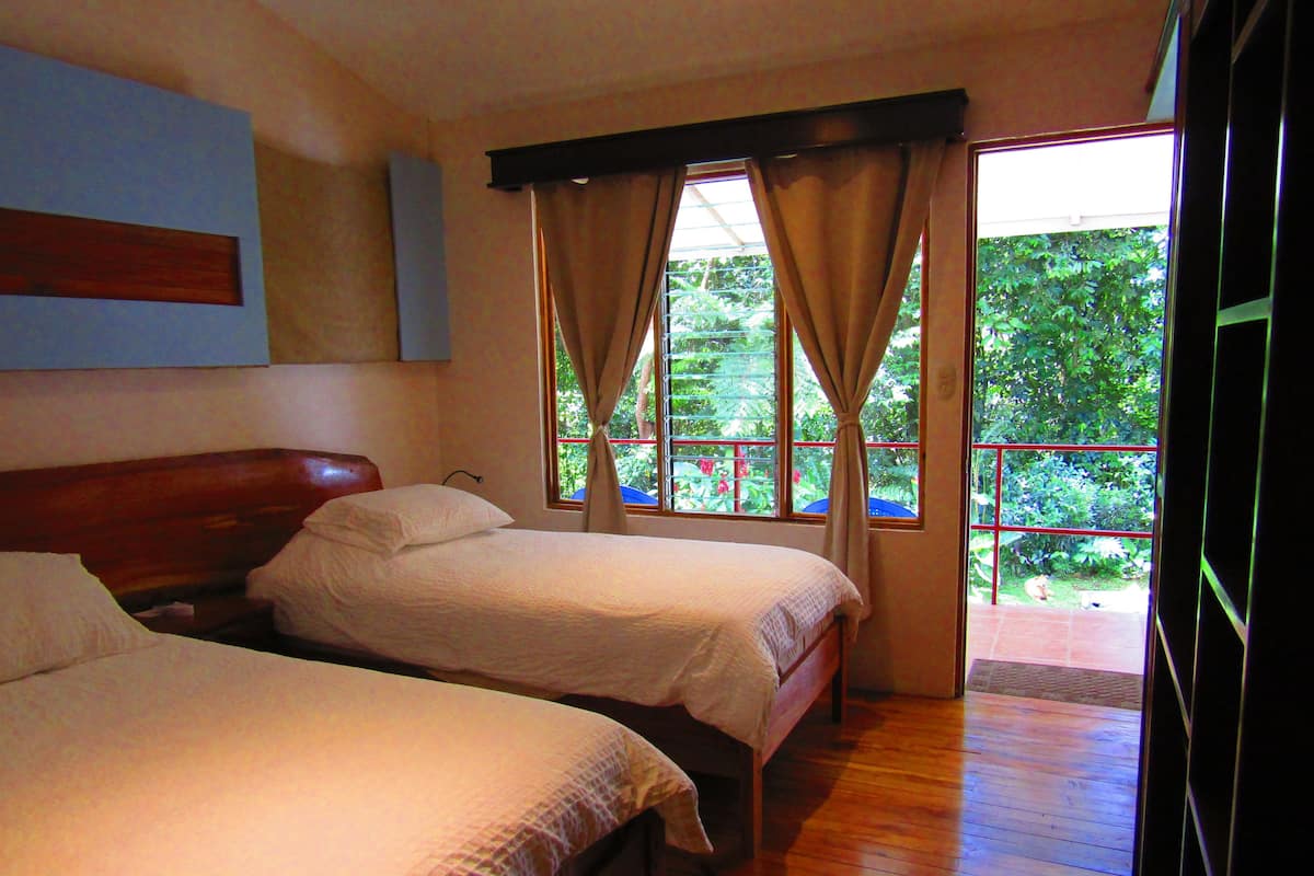 A room with two beds, wooden flooring, and a window with curtains.