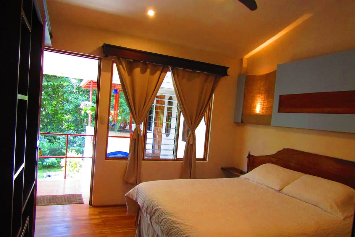 A bedroom with a large bed, a ceiling fan, and a window with curtains.
