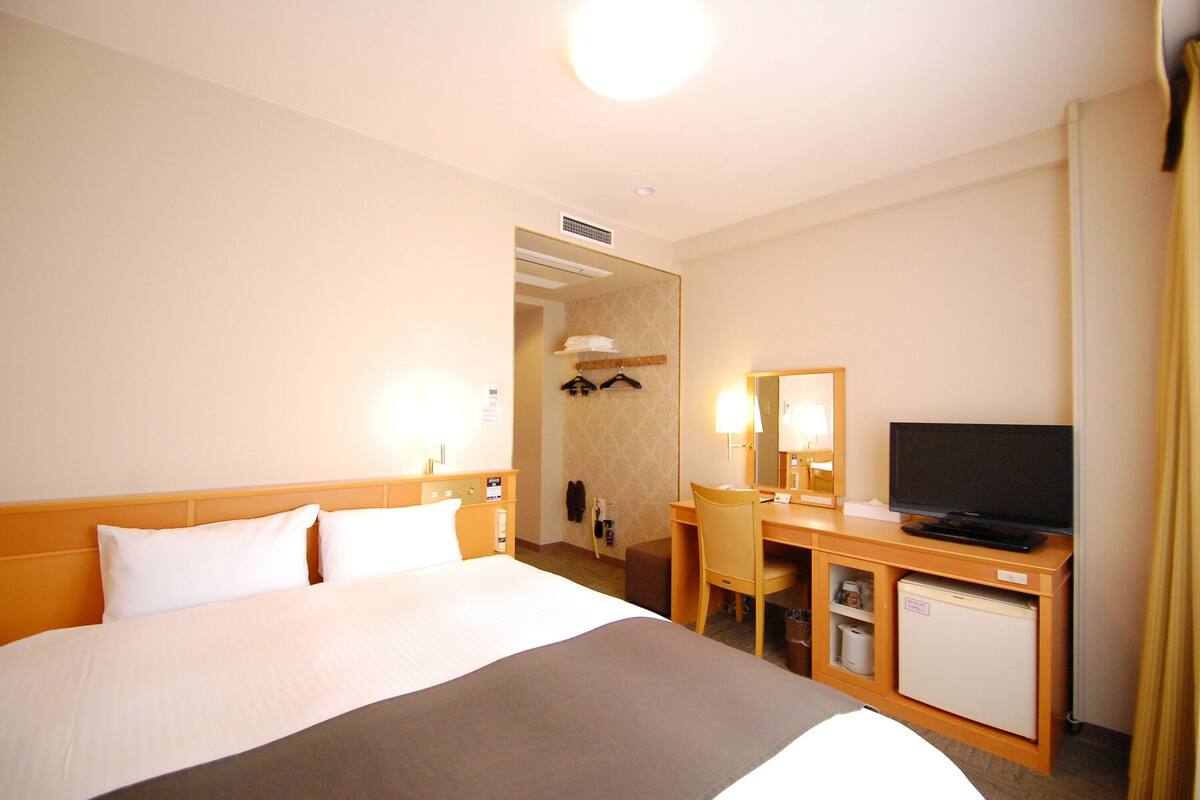 A hotel room with a large bed, a desk with a television, a small refrigerator, and a mirror.