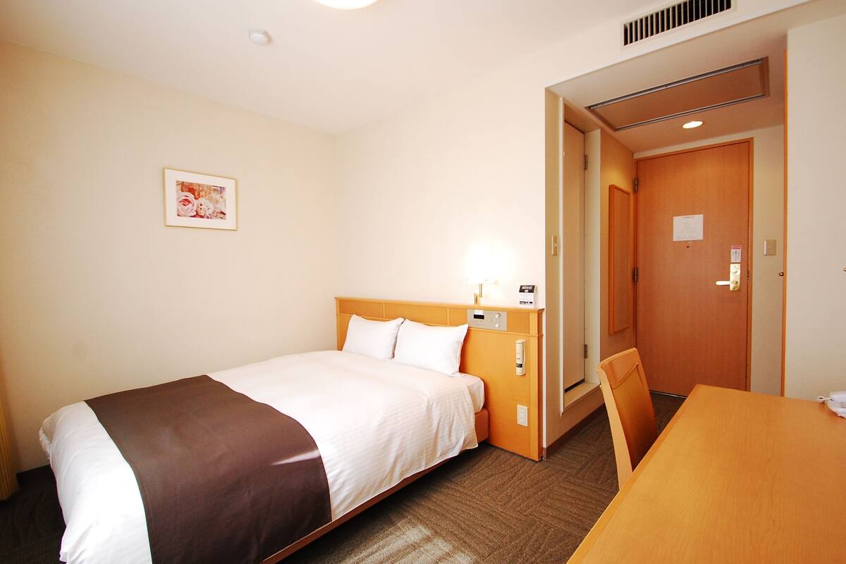 A hotel room with a bed, a desk, and a door.