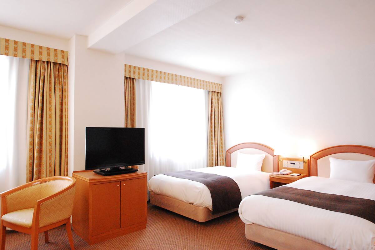 A hotel room with two beds, a television, a desk, and a chair.
