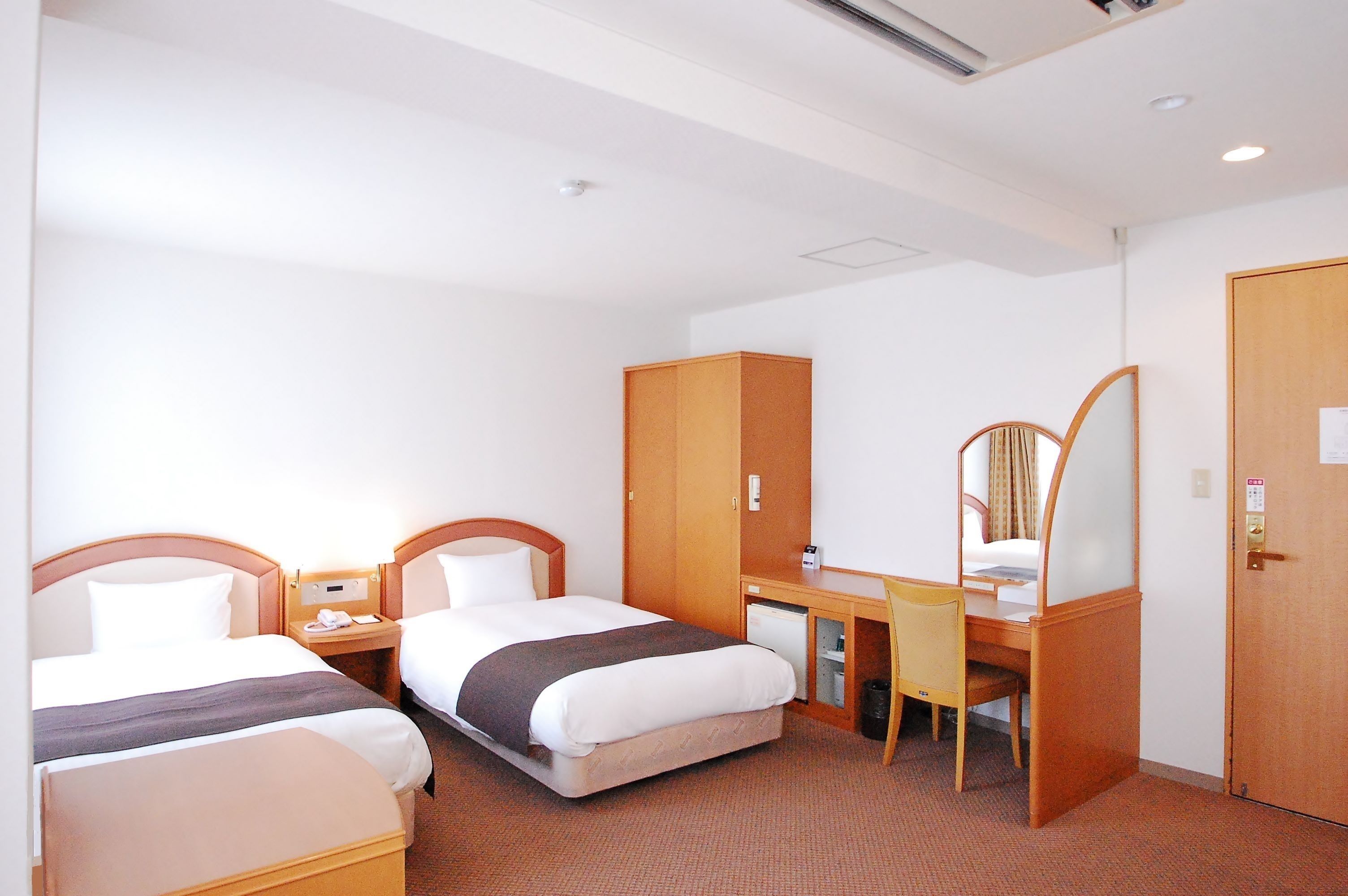 A hotel room with two beds, a desk, a chair, a wardrobe, and a mirror.