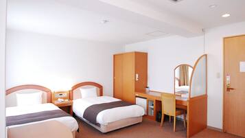 Habitación de hotel con dos camas, un escritorio, una silla, un armario y un espejo.