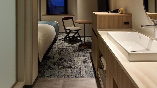 Quarto de hotel moderno com uma cama grande, uma penteadeira de madeira, um espelho amplo e uma pequena escrivaninha com cadeira.