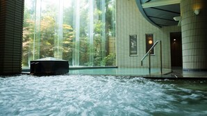 Un área de aguas termales con vistas a árboles a través de amplios ventanales, un jacuzzi y suelo de baldosas.