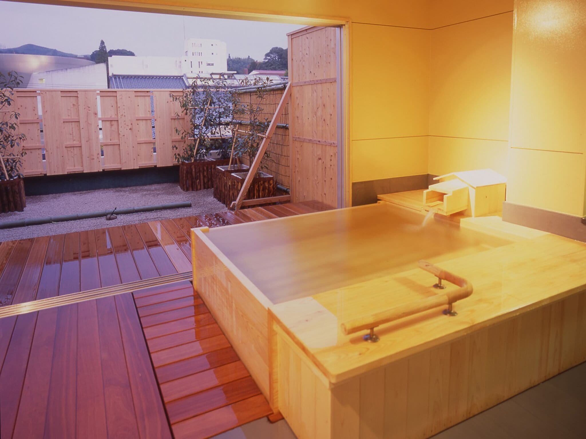 Una bañera de hidromasaje de madera con una terraza de madera y vistas a edificios al fondo.