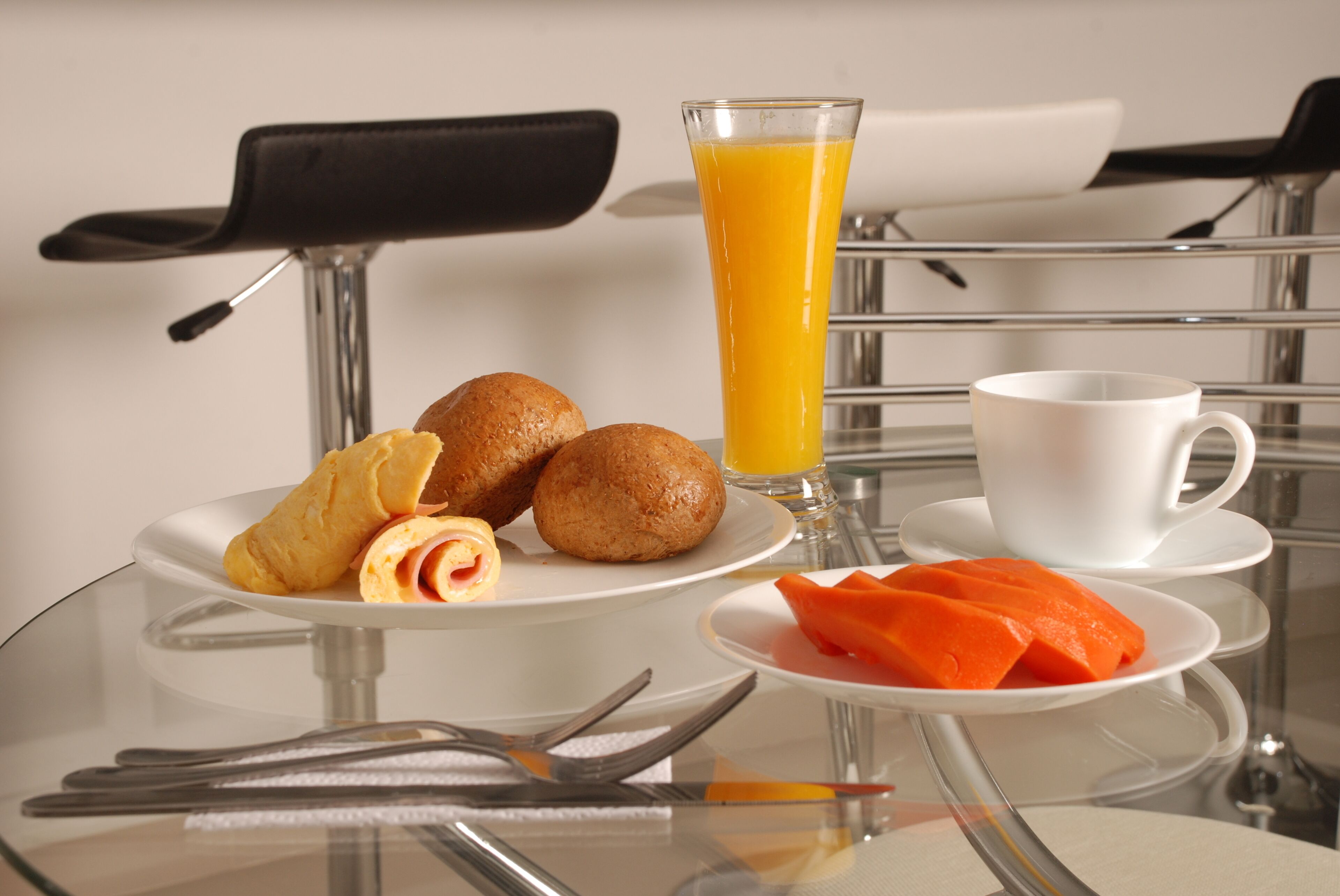 Un desayuno con cruasanes, zumo de naranja y una taza blanca sobre una mesa de cristal.