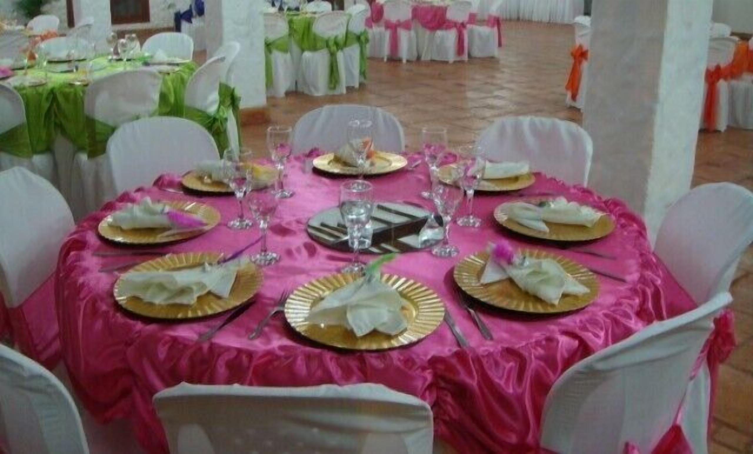 Un tavolo rotondo apparecchiato per un evento formale, con sedie bianche e una tovaglia rosa.