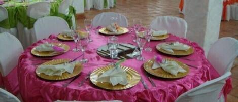 Un tavolo rotondo apparecchiato per un evento formale, con sedie bianche e una tovaglia rosa.