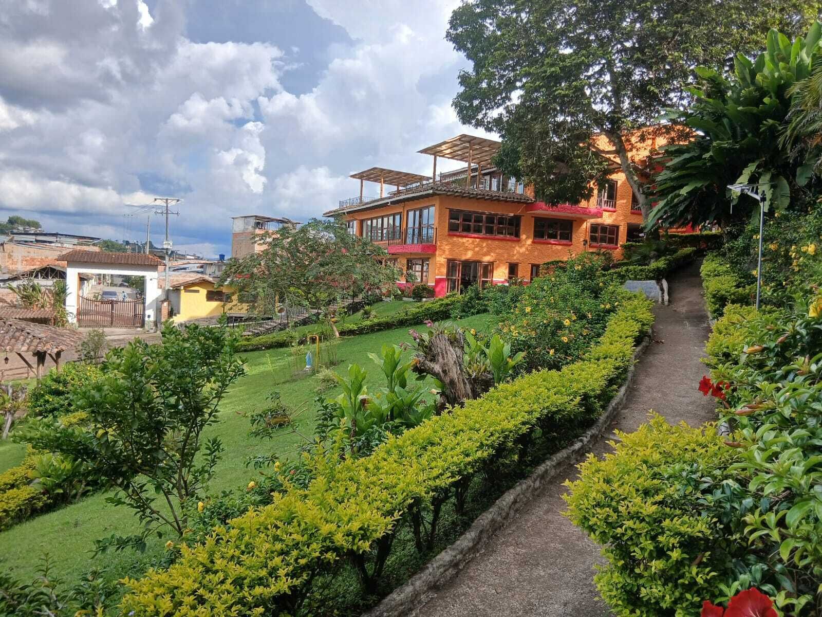 Un exuberante jardín con un sendero que conduce a un edificio con amplias ventanas y un espacio al aire libre cubierto.