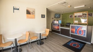 A motel lobby with a reception desk, a small seating area with two tables and four chairs, and a few informational posters on the walls. - Motel 6 New Iberia, LA (New Iberia)