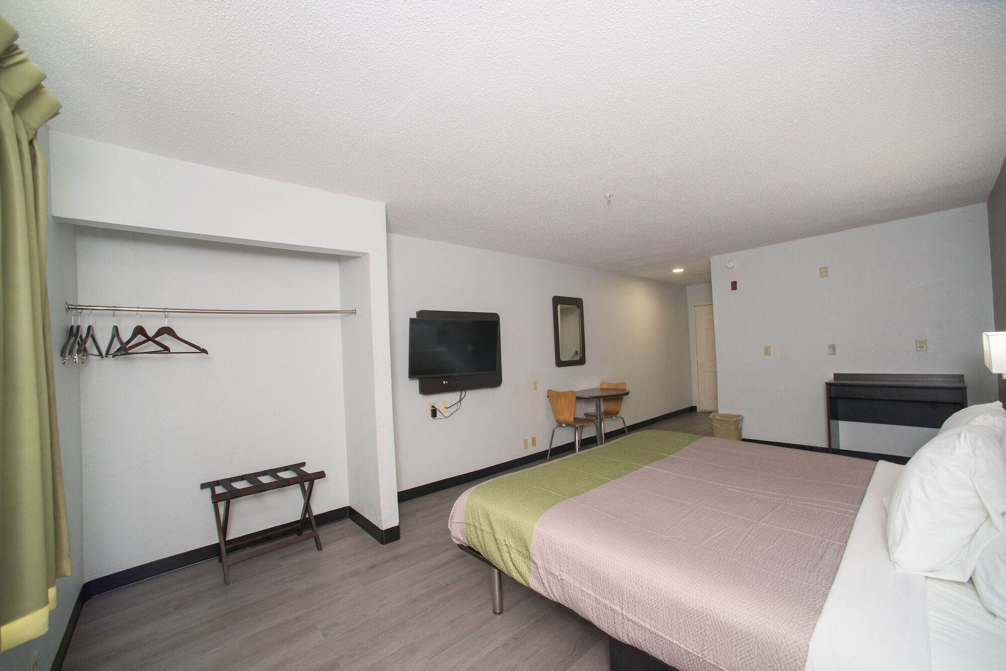 Habitación de hotel con cama, una mesita con sillas, televisor montado en la pared y perchero con ganchos.