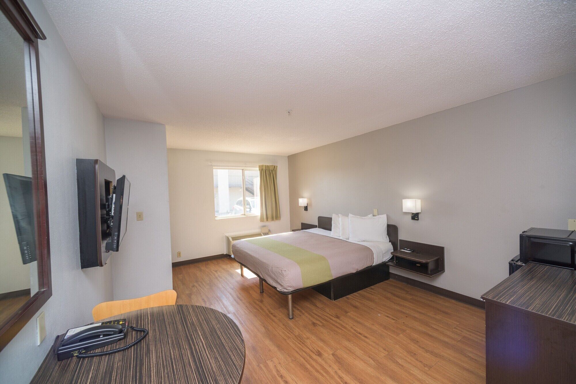 A hotel room with a bed, bedside tables, a desk, a chair, a telephone, and a window with curtains.