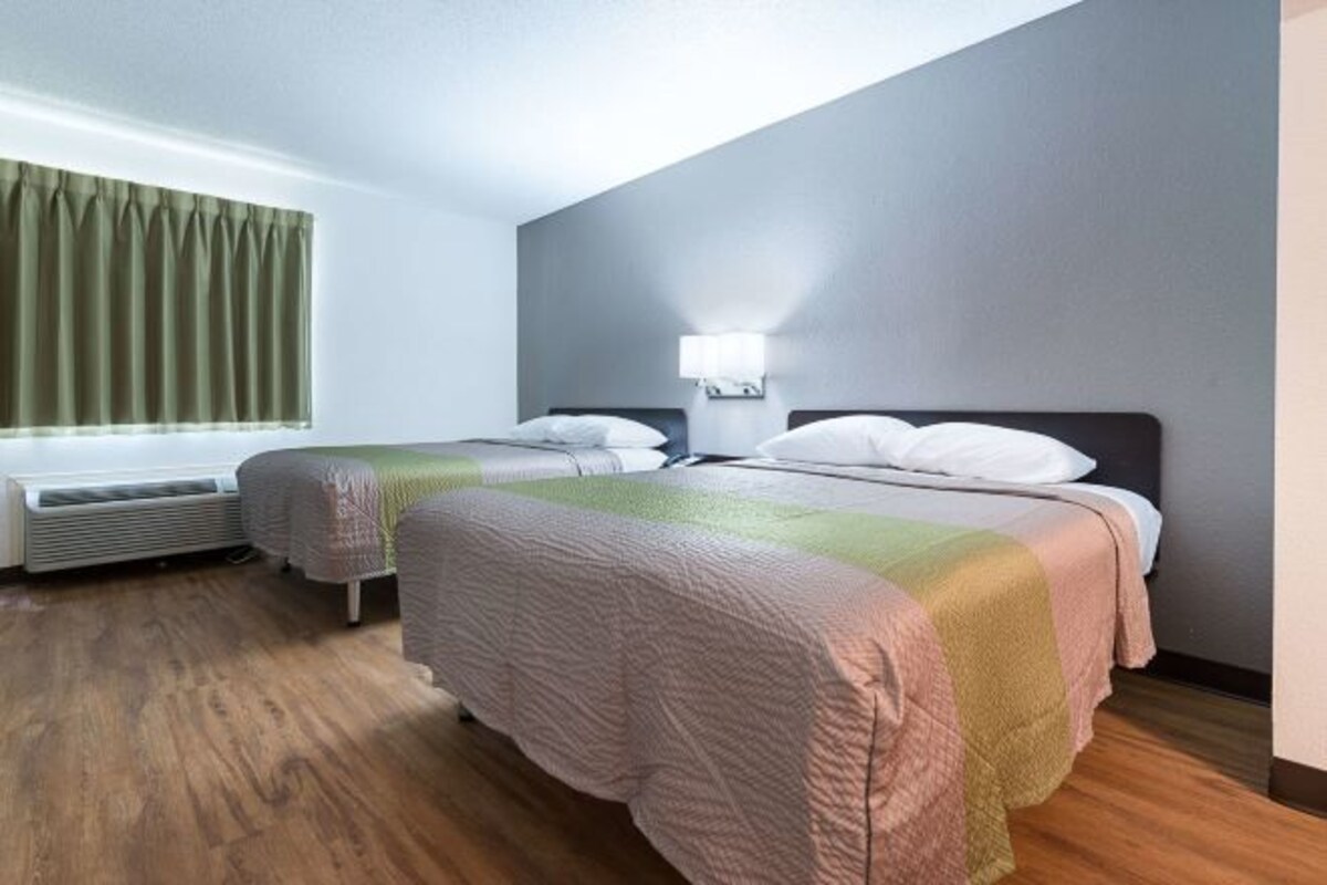 Quarto de hotel com duas camas, janela com cortinas, luminária na parede e radiador.