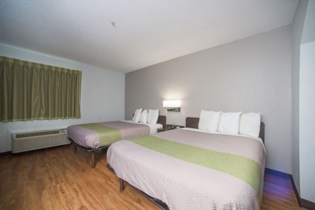 Quarto de hotel com duas camas, janela com cortinas, luminária fixada na parede e ar condicionado.
