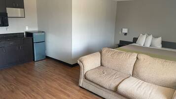 Una habitación de hotel con kitchenette, una cama con ropa de cama blanca y un sofá color beige.