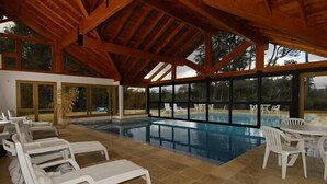 Una piscina interior con sillas de descanso y una mesa, rodeada de amplios ventanales.