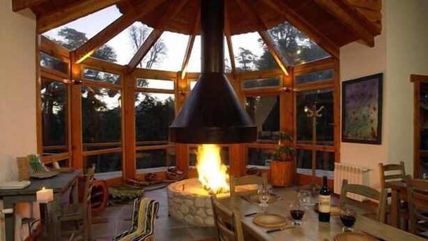 Un comedor acogedor con chimenea de piedra, muebles de madera y amplios ventanales que dejan entrar luz natural.