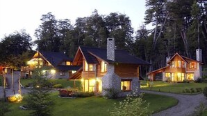 Una cabaña de estilo rústico con varias habitaciones, rodeada de un jardín cuidado y zona boscosa.