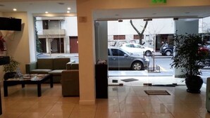 A hotel lobby with a reception desk, seating area, and a view of parked cars outside. - Posta del Viajante (Mar del Plata)