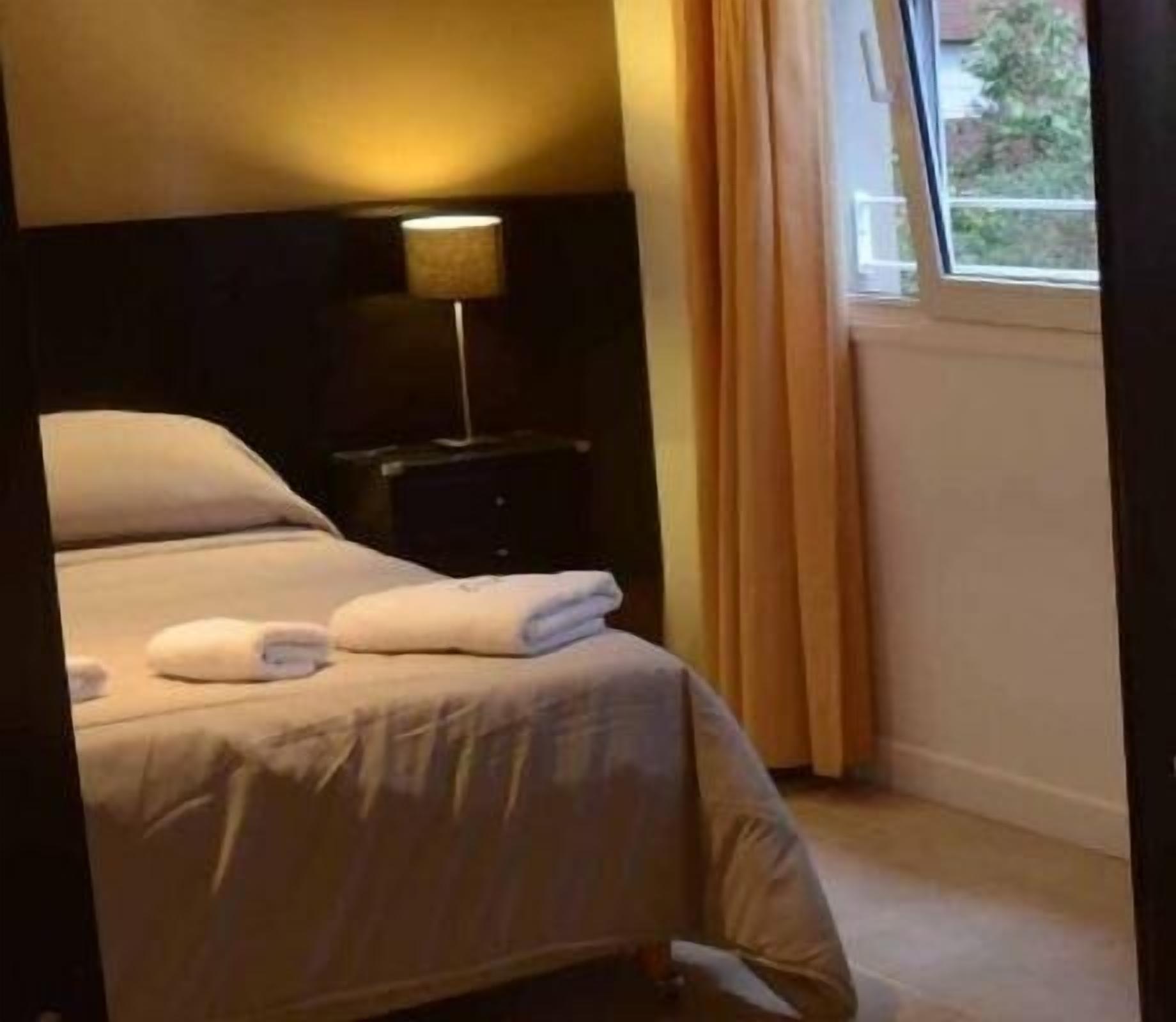 Ein Hotelzimmer mit Bett, Nachttisch, Lampe und einem Fenster mit Vorhängen.
