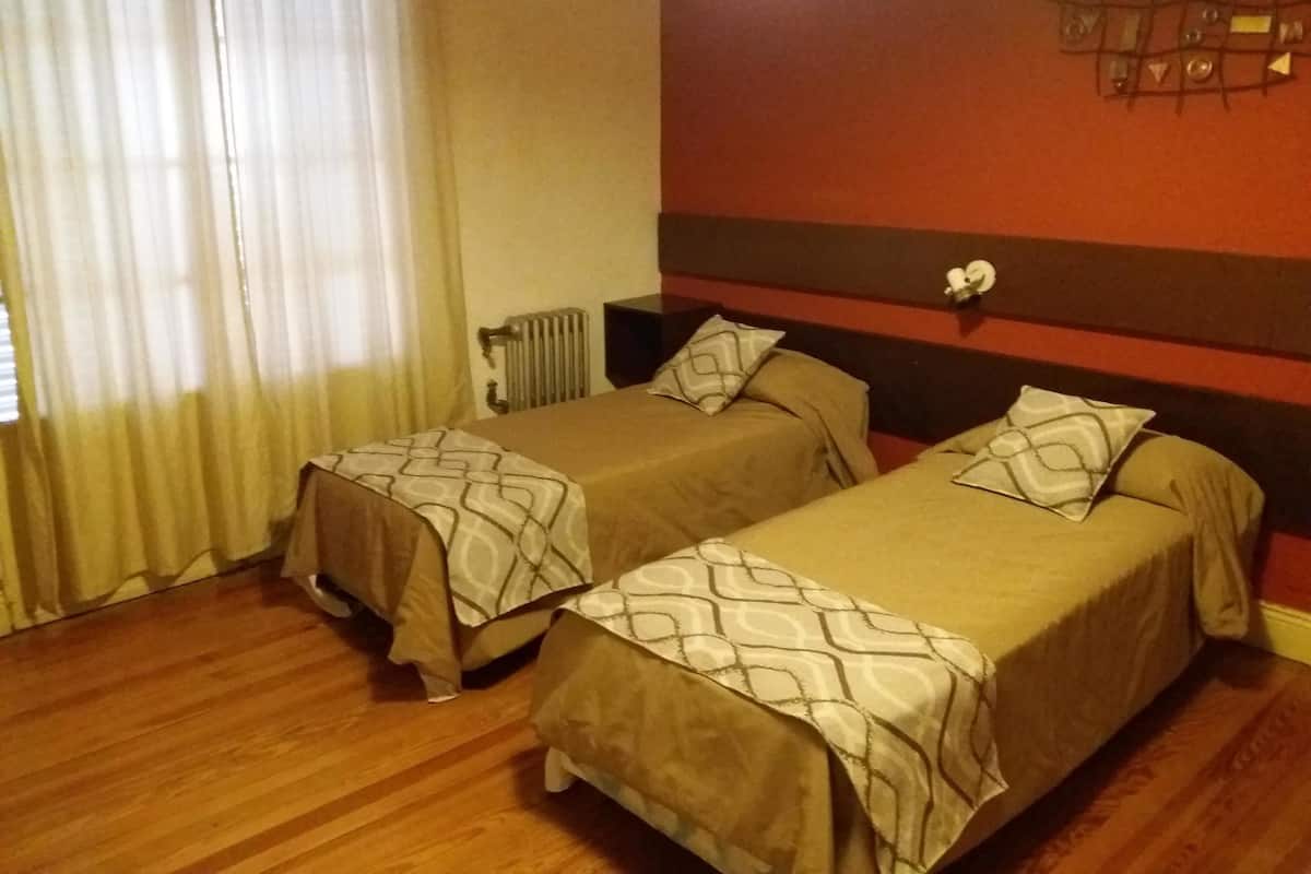 Ein Hotelzimmer mit zwei Einzelbetten, einem Heizkörper, einem Fenster mit Vorhängen und einer Wand mit einem geometrischen Muster.