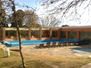 Zona de piscina con sillas de descanso y un edificio con grandes ventanales.
