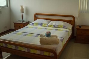 A neatly made bed with a checkered bedspread, a bedside lamp, and a small bedside table with a cup.