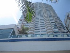 A high-rise building with multiple balconies and a palm tree in the foreground.