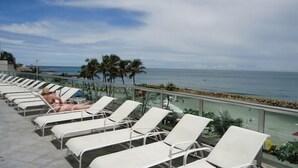 A sun deck with white lounge chairs and a glass railing overlooking the ocean. - Apartamento Edificio Palmetto 2301 - Arriendos IH (Cartagena de Indias)