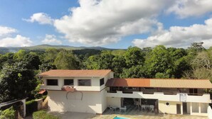 Un edificio de dos pisos con techo de tejas, un patio cubierto y una piscina.