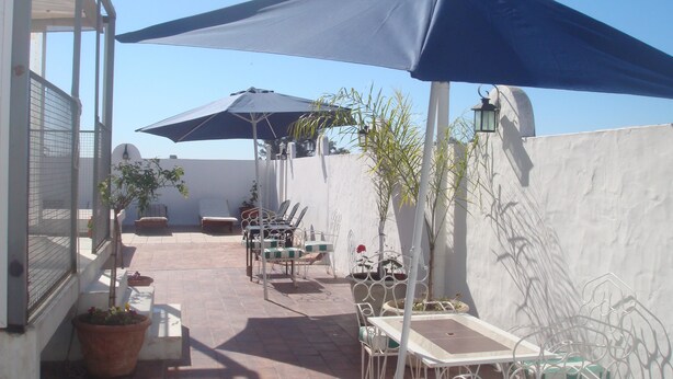 Een terras buiten met een tafel, stoelen, twee parasols en planten in potten.