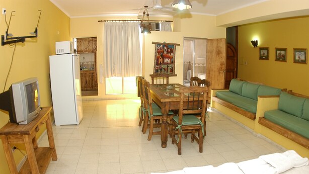 A compact living space with a dining area, a green sofa, a wooden table, and a white refrigerator. - Adamo Apart (San Rafael)