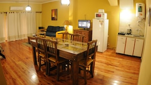 A dining area with a wooden table and chairs, a television, and a kitchen area with a refrigerator and microwave. - Adamo Apart (San Rafael)