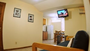 A small, cozy room with a bed, a television mounted on the wall, a kitchen area with cabinets and a refrigerator, and framed pictures on the wall. - Adamo Apart (San Rafael)
