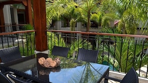 A glass-top table with four chairs, surrounded by lush greenery and a wooden railing. - Macaws Jaco Condos No.12 (Jaco)