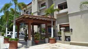 A multi-story building with a covered entrance area, potted plants, and a car parked outside. - Macaws Jaco Condos No.12 (Jaco)