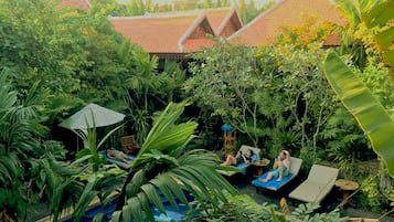 A lush garden with a swimming pool, lounge chairs, and a traditional building with a tiled roof.