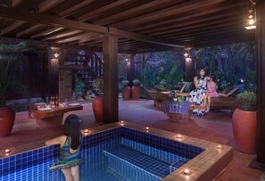 Un área de piscina con suelo de baldosas, una terraza de madera y un espacio de estar con mesa y sillas.